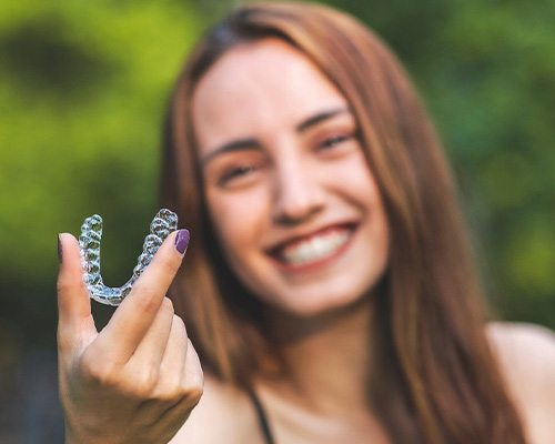 A smiling woman holding an Invisalign tray outdoors