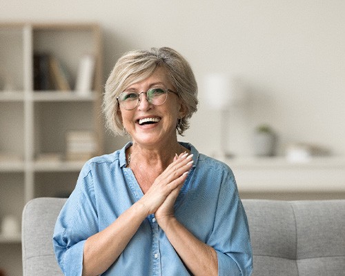 Senior woman with glasses smiling on couch at home