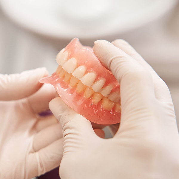Gloved hands holding full dentures