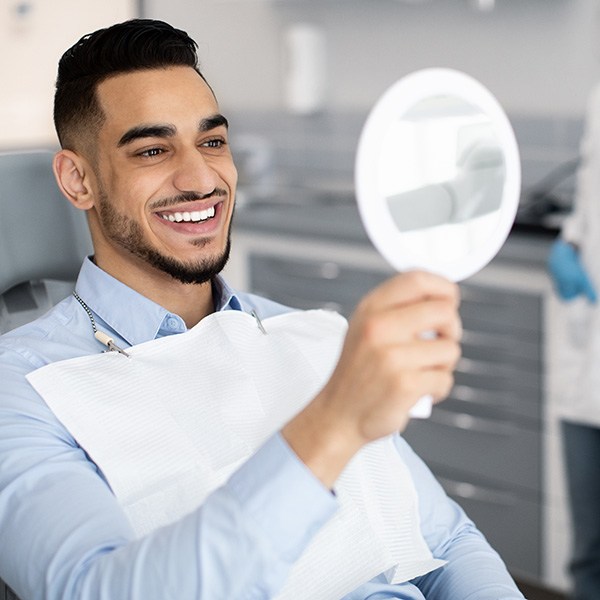 Man smiling at reflection in handheld mirror